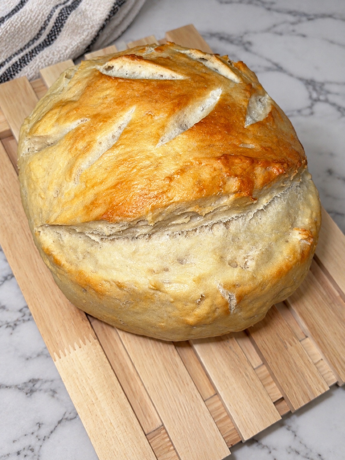A golden round loaf of Sagit's fresh bread with a scored crust, resting on a wooden board
