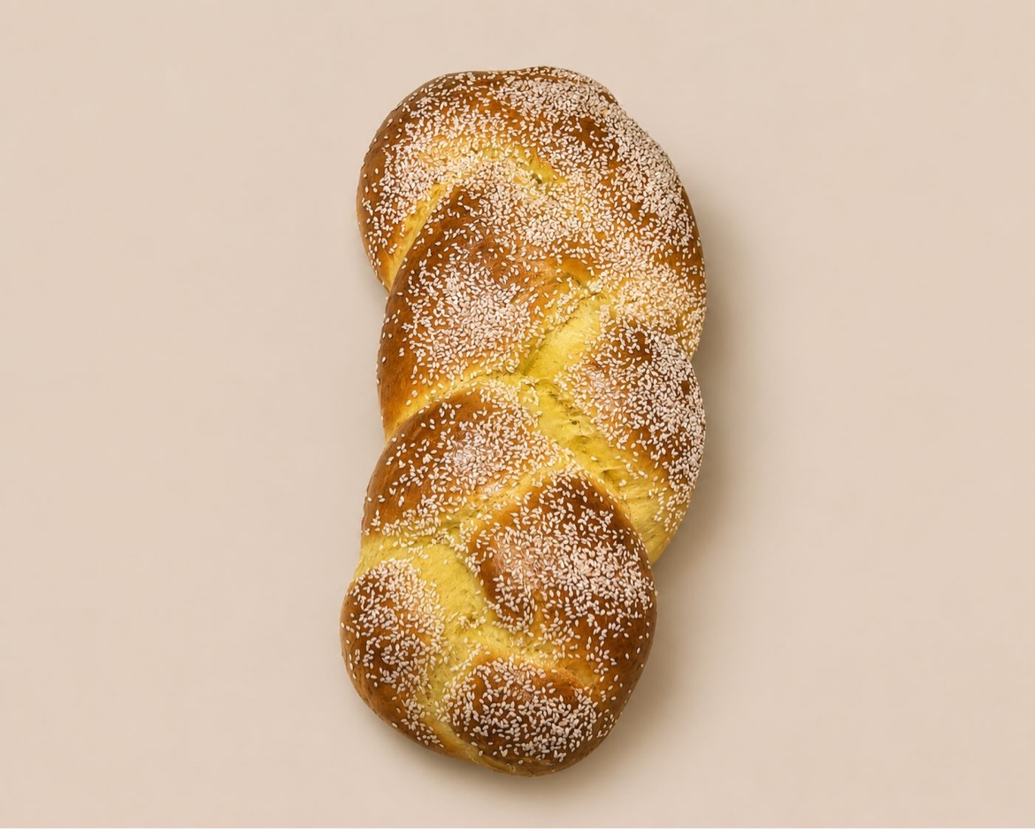 Golden braided challah topped with sesame seeds on a cream background
