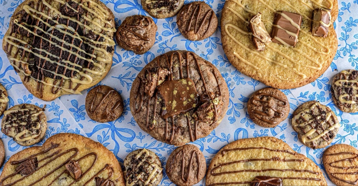 Flat lay of Sagit's loaded cookies with chocolate drizzle, Oreo pieces and Kinder Bueno on blue floral paper